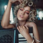 Self assured young female singer with curly hair and makeup standing in modern studio with synthesizer before concert