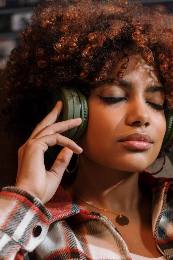 Portrait of a woman with curly hair relaxing with headphones on, eyes closed.